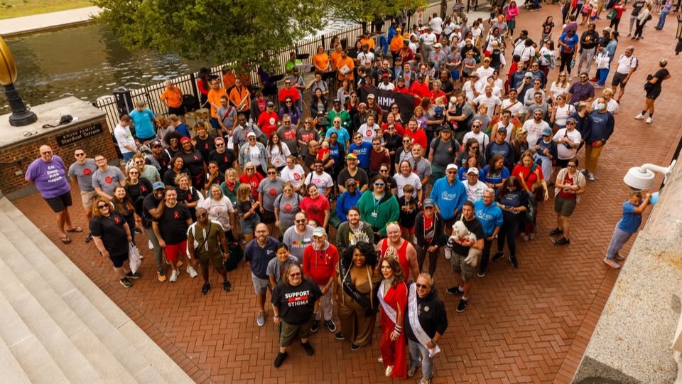 Large group of people standing on a brick plaza in front of the Downtown Canalwalk in Indianapolis.