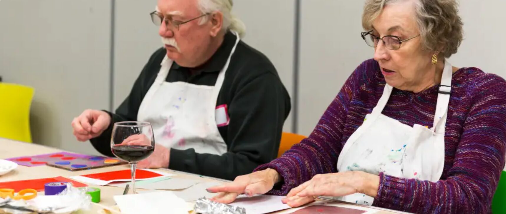 Two people with painting aprons on sitting at a table crafting.