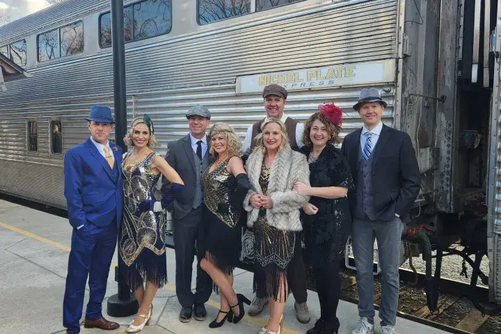 men and women dressed in 1920s attire pose in front of a train